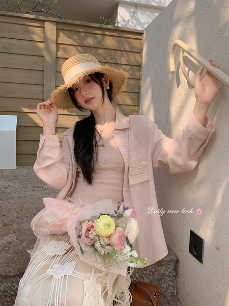 Woman wearing a light pink summer outfit with a straw hat and bouquet