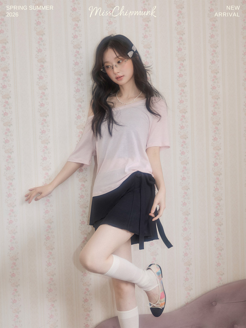 Female model wearing a pastel pink top, black wrap skirt, socks, and flats