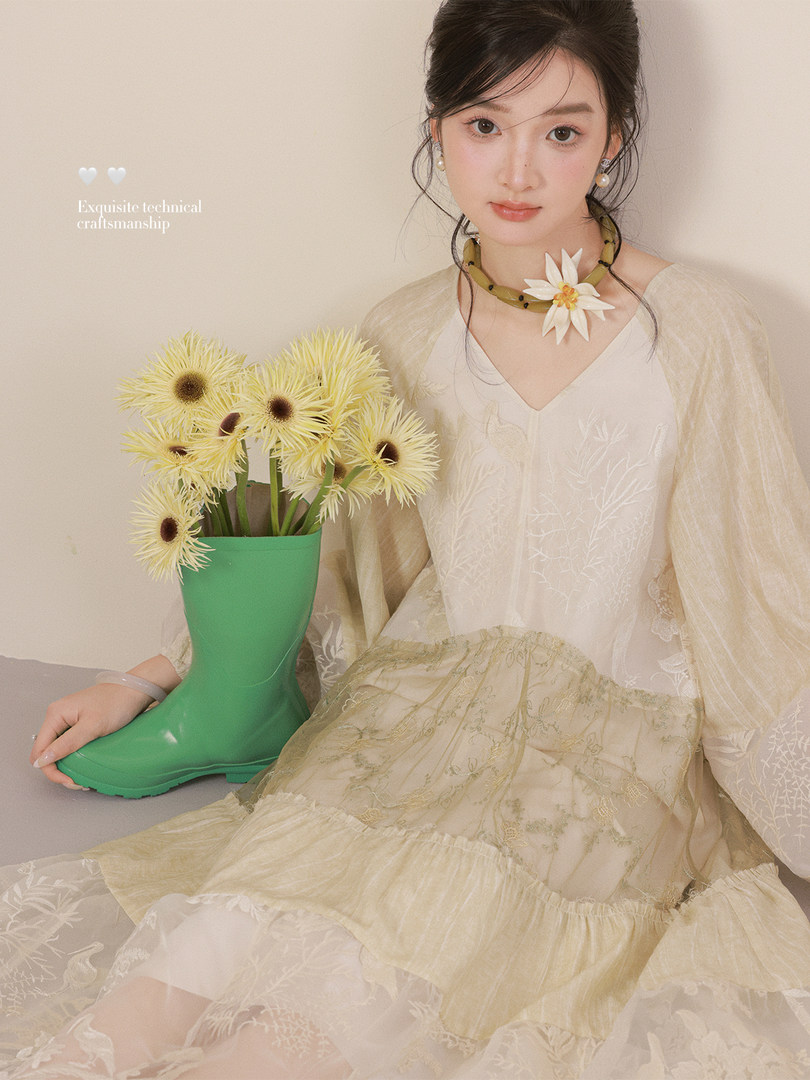Model wearing a cream embroidered dress with a green boot and floral accessory