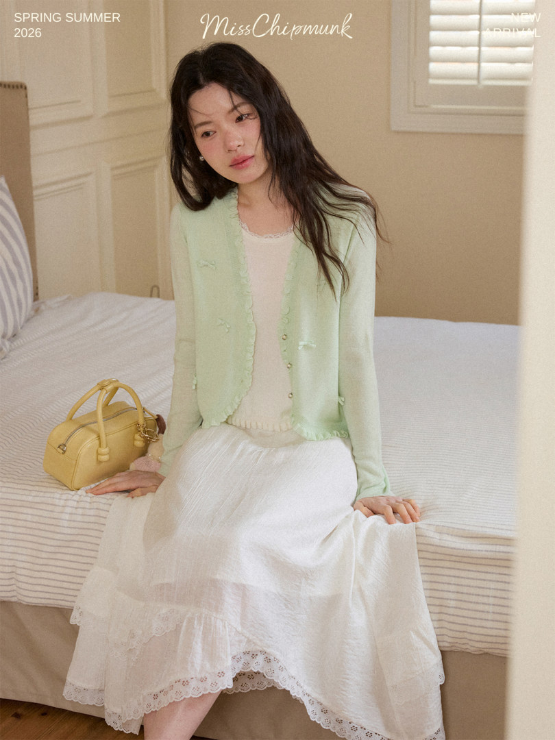 Model wearing a pastel green cardigan and white lace skirt with a yellow handbag
