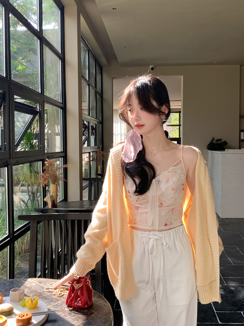 Woman wearing a floral camisole, cream cardigan, and white pants