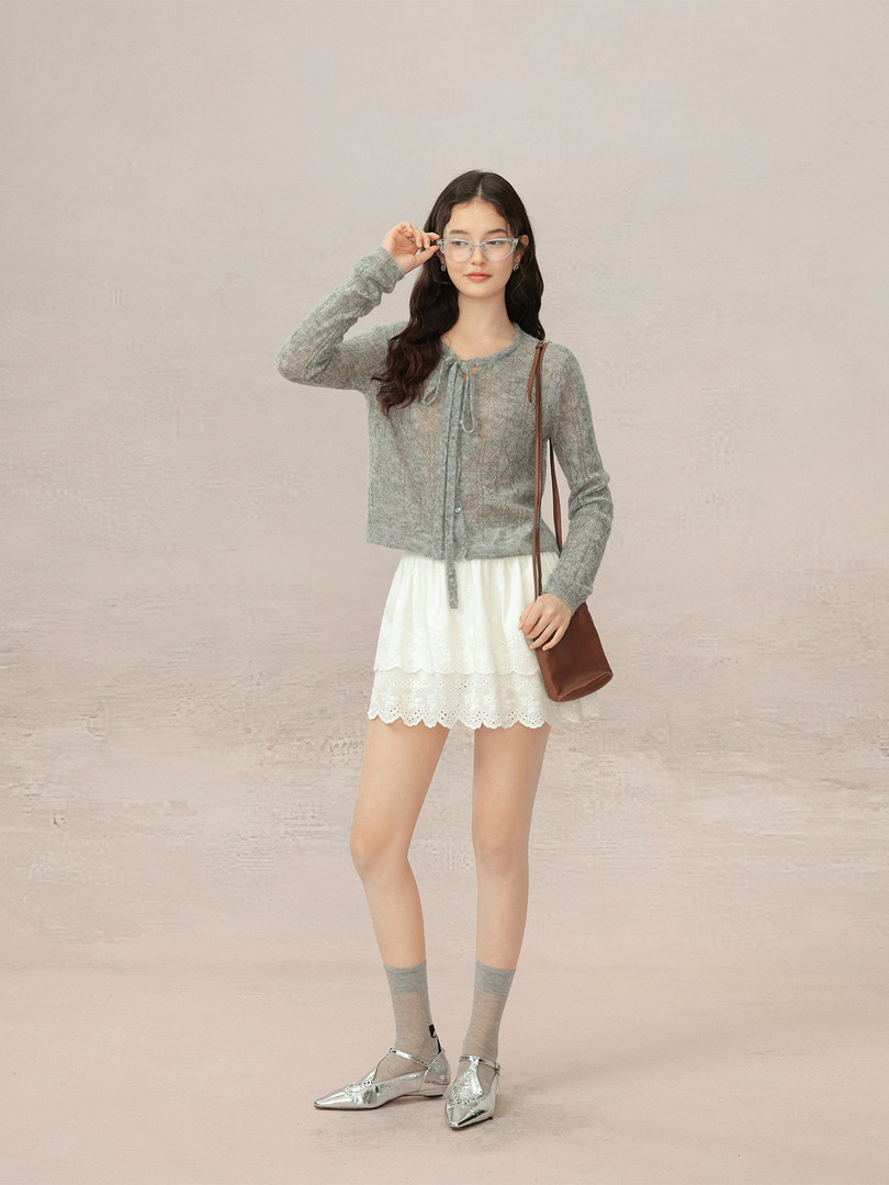 Model wearing a gray sheer cardigan, white lace skirt, silver flats, and brown crossbody bag