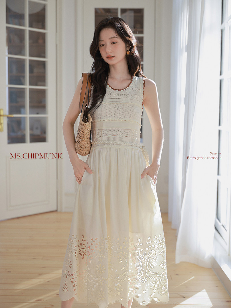 Model wearing a cream sleeveless embroidered maxi dress with a woven bag