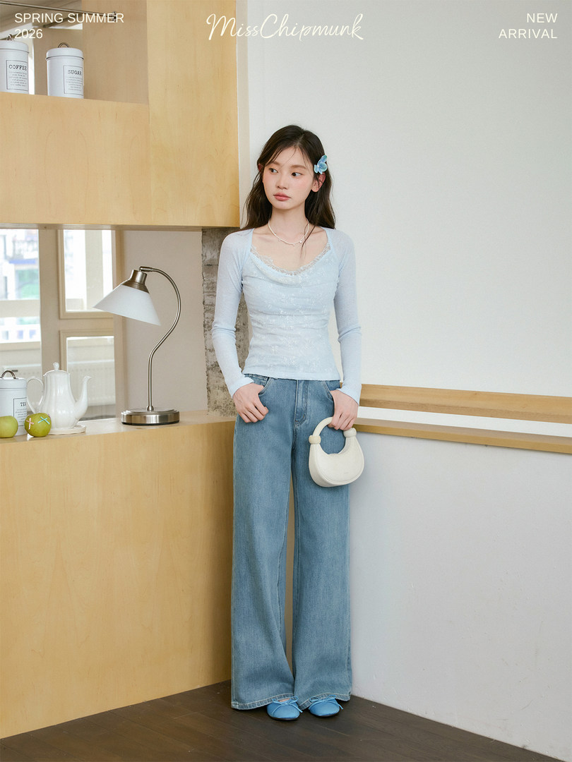 Model wearing a light blue long-sleeve top with wide-leg jeans and a small white handbag