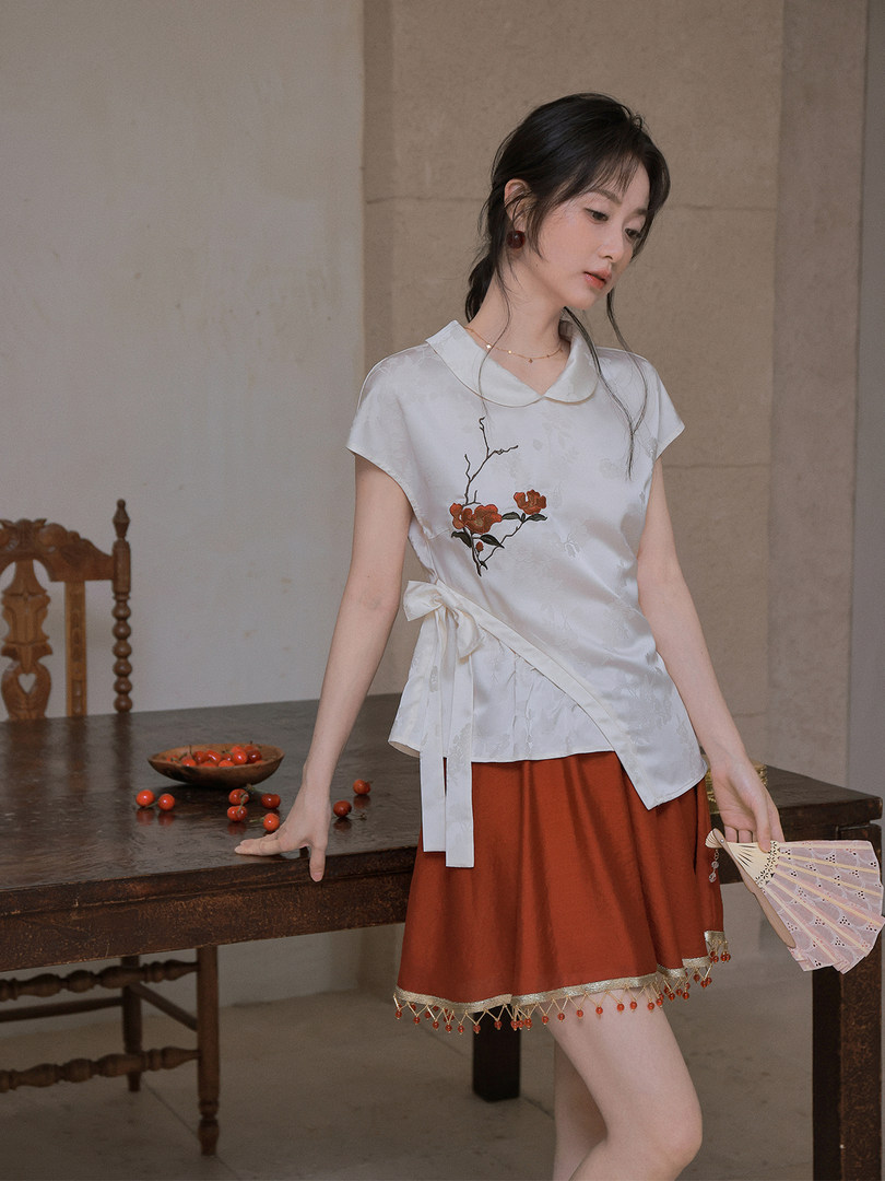 Model wearing a white embroidered wrap blouse with a rust-colored skirt