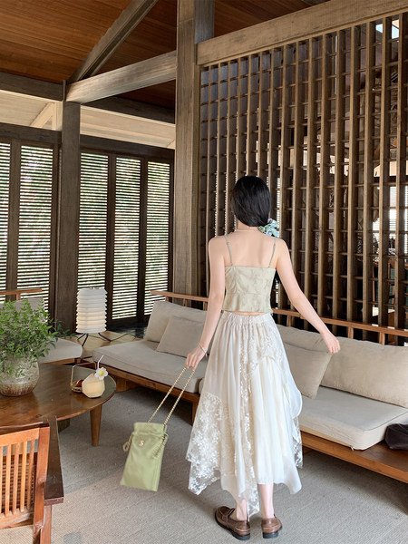 Woman wearing a light green camisole top and white lace midi skirt indoors