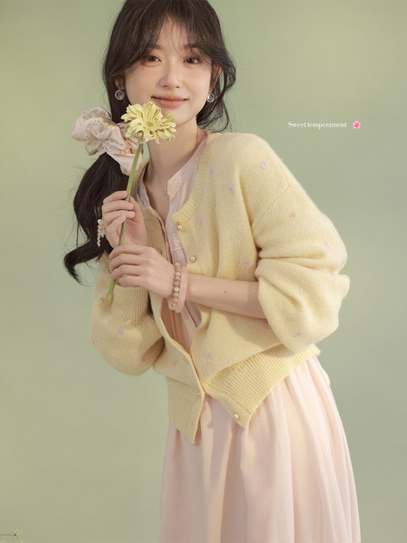 Woman wearing a pastel yellow cardigan over a pink dress while holding a flower