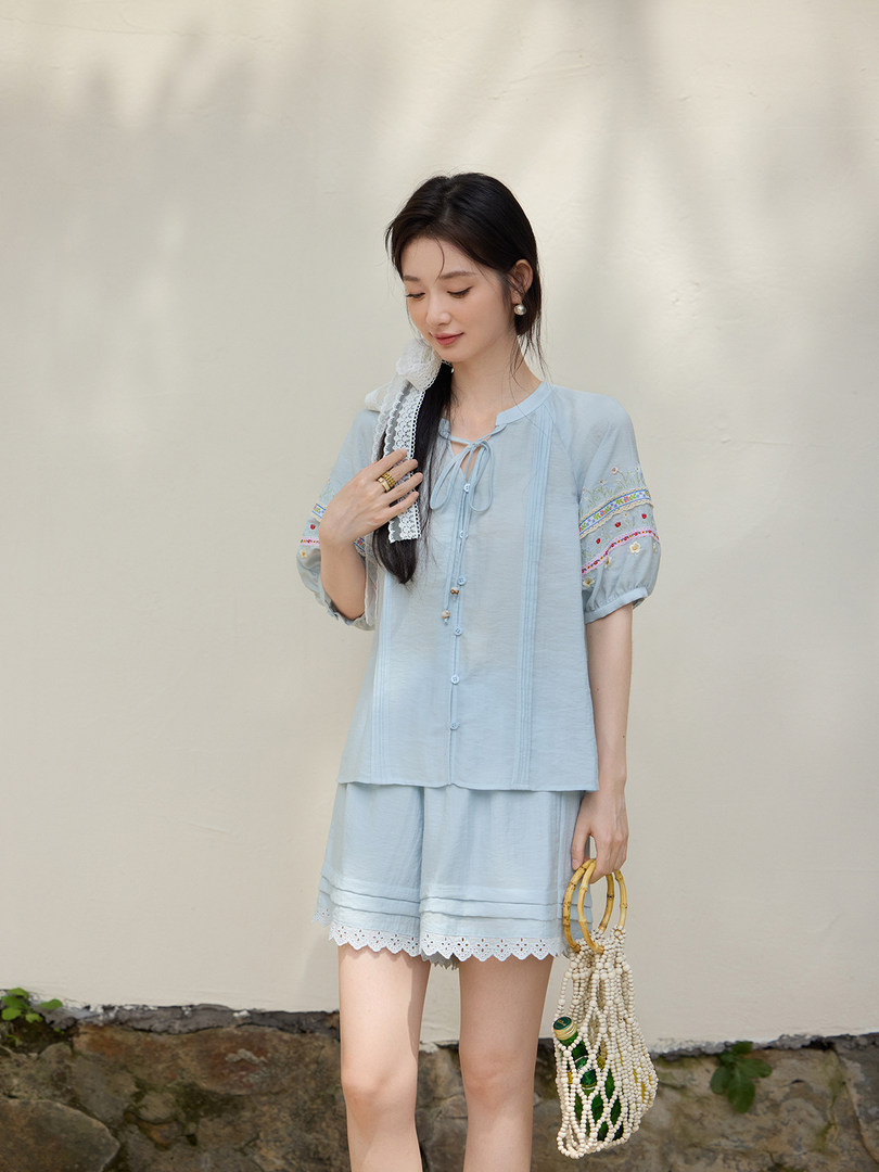 Model wearing a light blue embroidered two-piece summer outfit with a beaded handbag