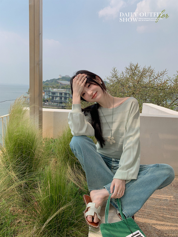Woman wearing a light green long-sleeve top and jeans outdoors with a green bag