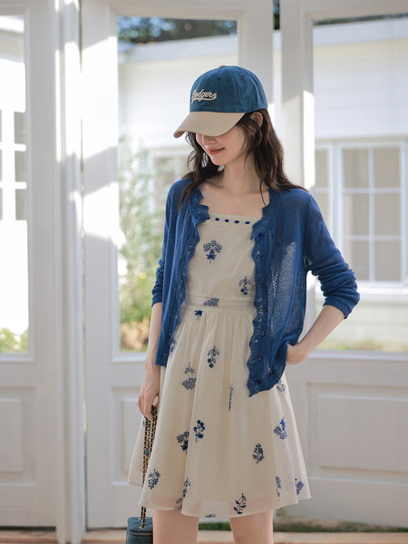 Woman wearing a cream floral dress with a blue cardigan and baseball cap