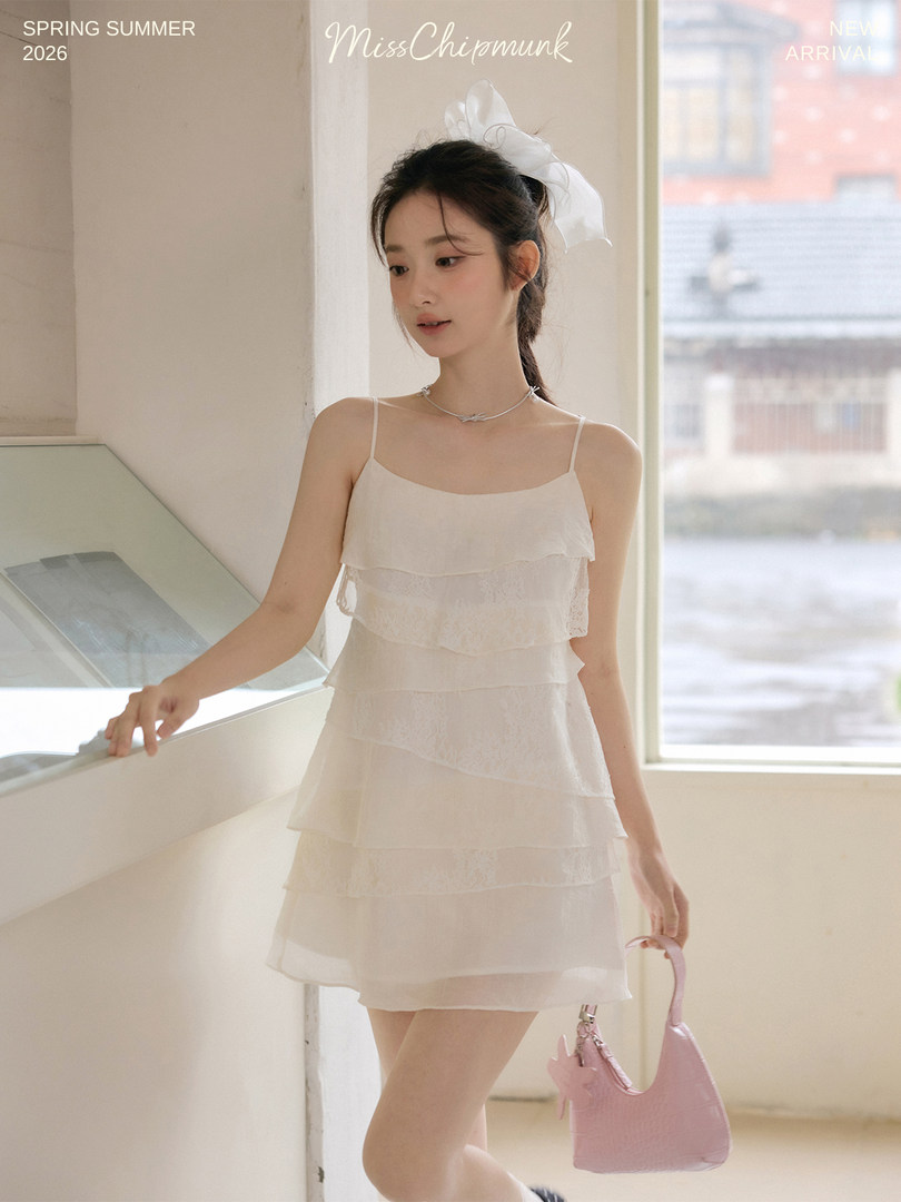 Model wearing a white layered spaghetti-strap dress with a pink handbag