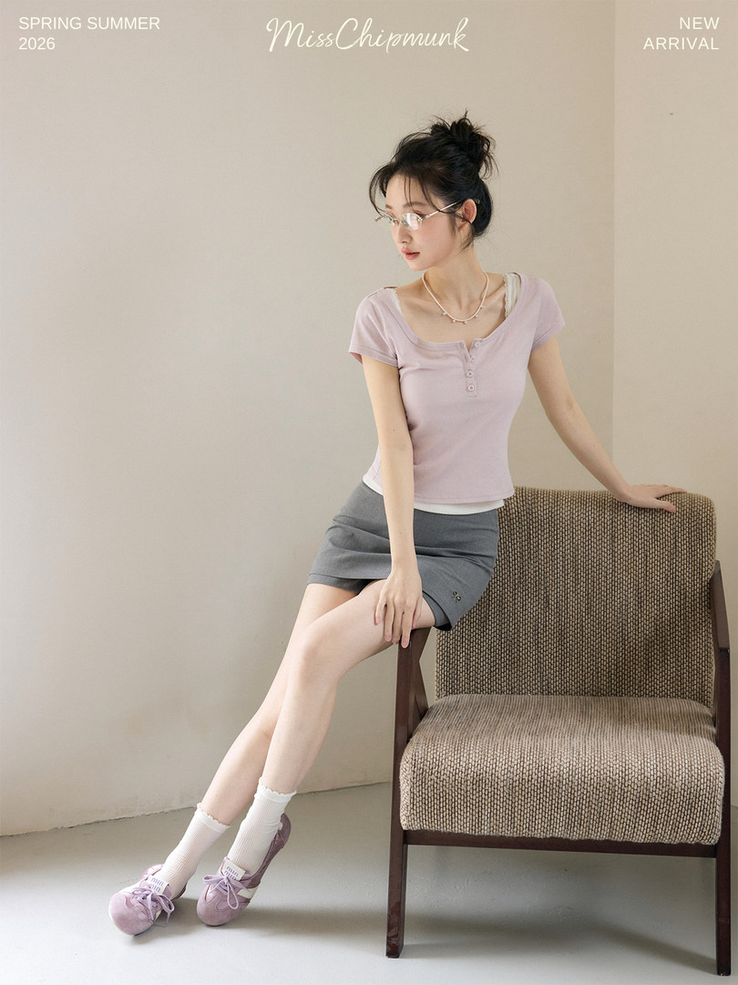 Model wearing a light purple short-sleeve top and gray mini skirt in a studio setting