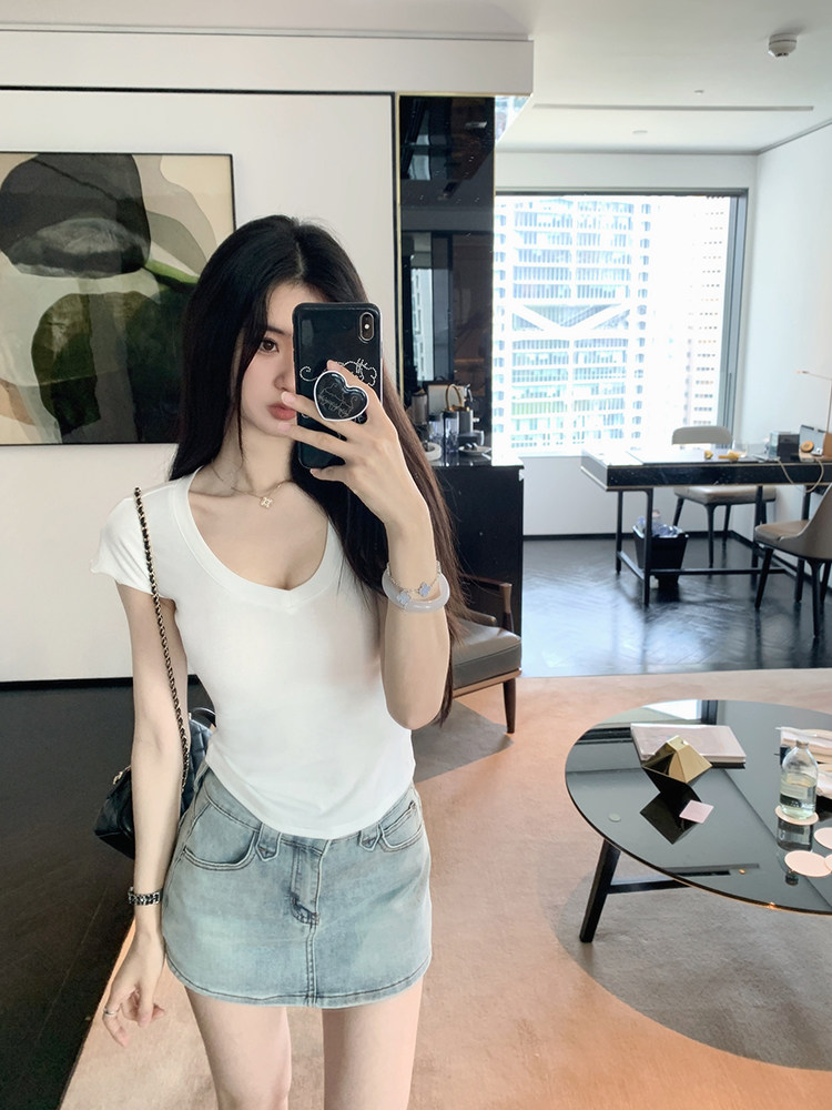 Woman taking mirror selfie wearing white top and denim skirt
