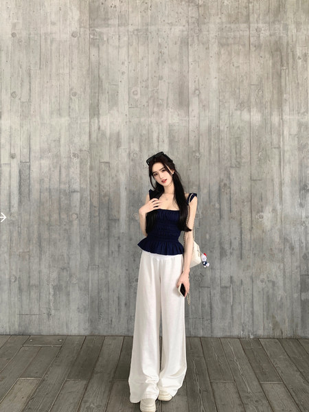 Woman wearing a navy blue peplum top and white wide-leg pants against a concrete wall background