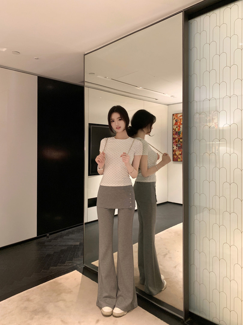 Woman wearing white polka dot top and gray wide-leg pants, posing in front of a mirror