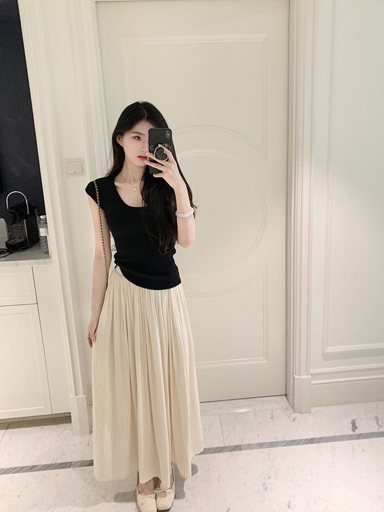 Woman wearing black sleeveless top and beige pleated skirt, taking mirror selfie