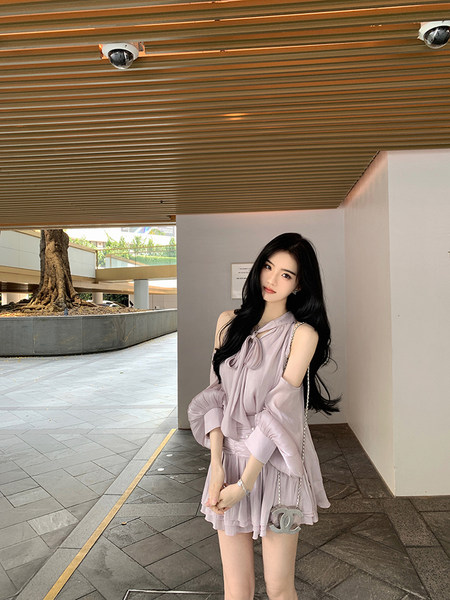 Woman wearing a light purple off-shoulder dress with ruffles, standing outdoors.