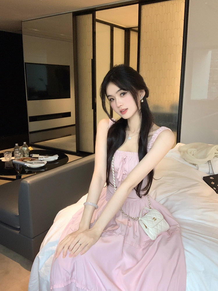 Woman wearing a pink dress sitting on a bed with a white handbag.