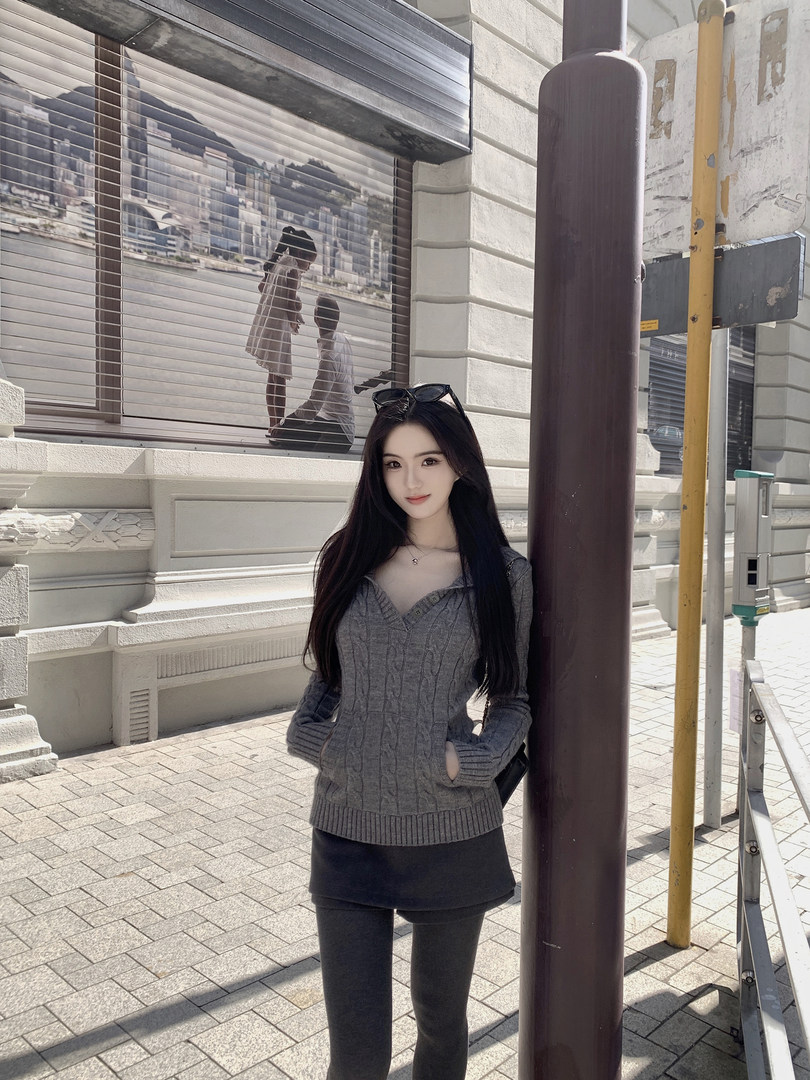 Woman wearing a gray cable-knit sweater and black skirt standing outdoors
