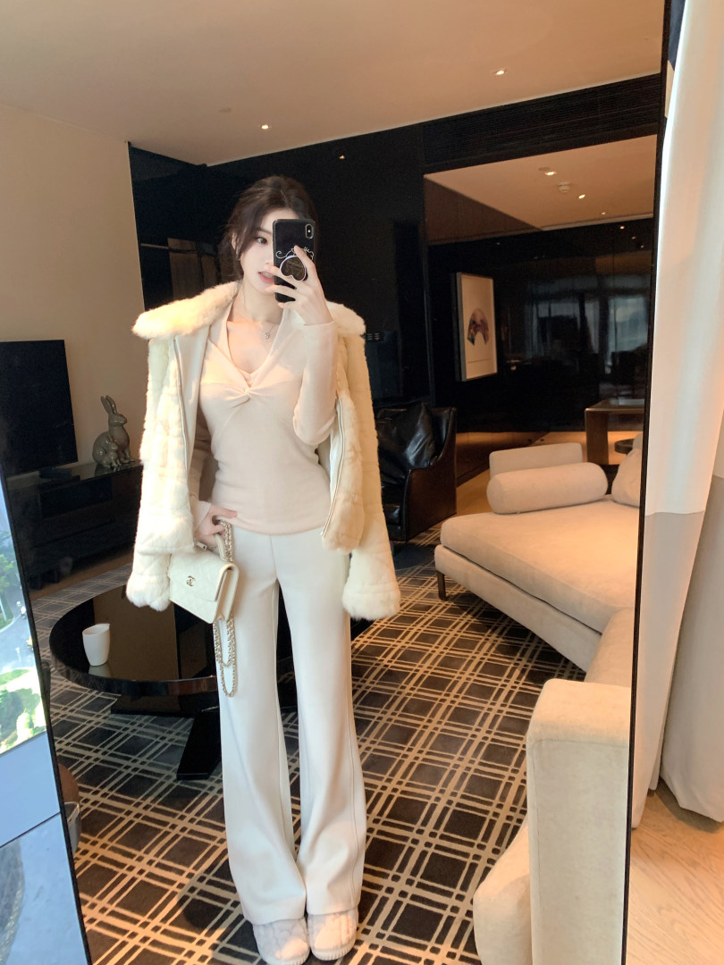 Woman taking mirror selfie wearing white outfit with fur coat and holding handbag