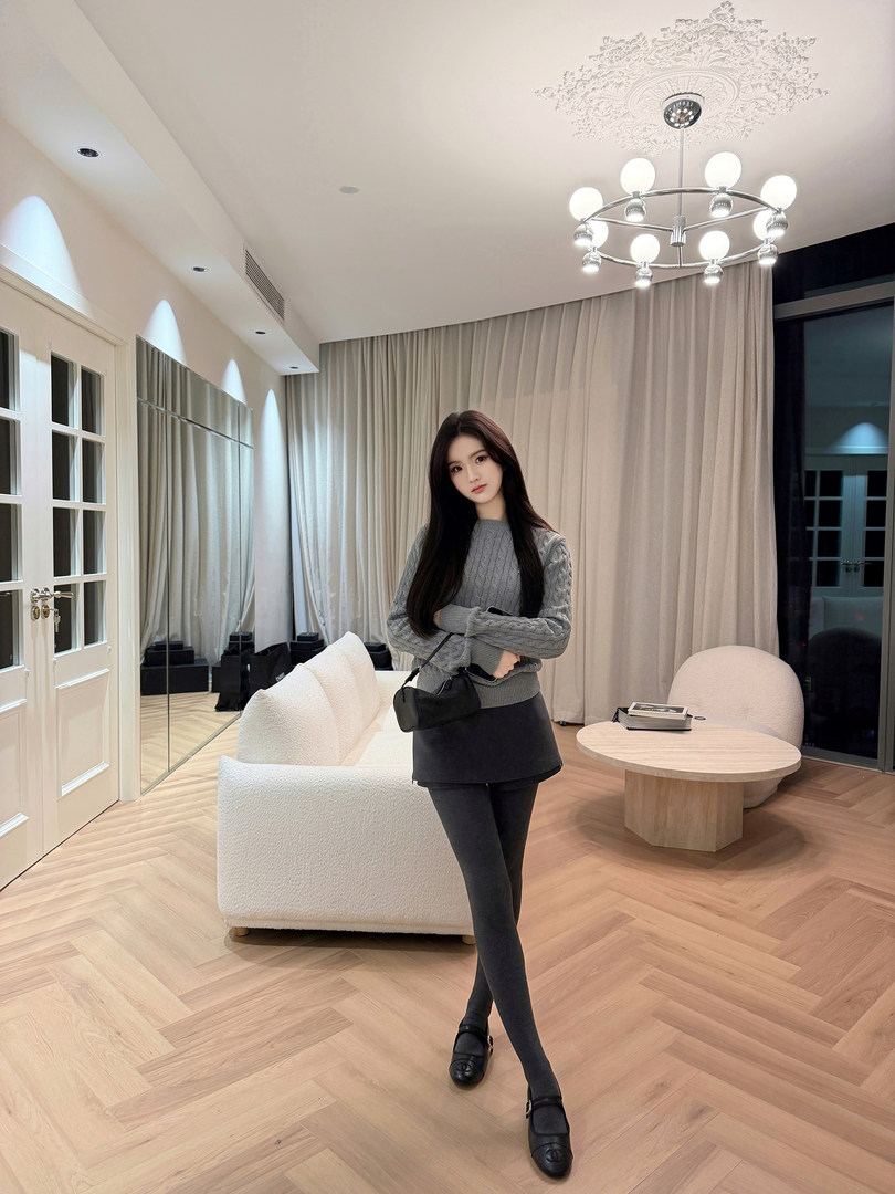 Woman modeling gray cable knit sweater, black mini skirt, and tights in a modern living room