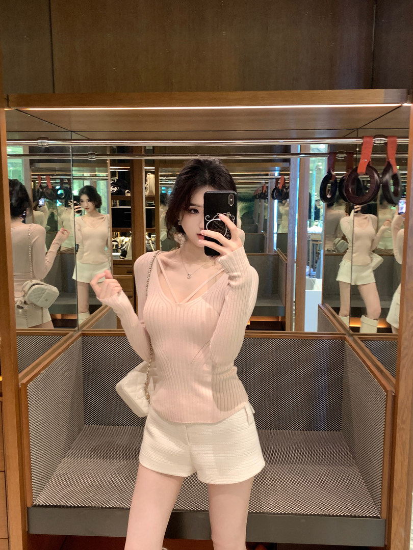 Woman taking mirror selfie wearing a light pink ribbed long-sleeve top and white shorts in a store fitting room