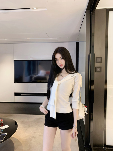 Woman wearing a white knitted top with a bow and black shorts, accessorized with a chain bag.