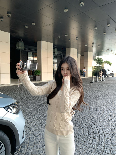Woman wearing a cream cable-knit sweater taking a selfie outdoors.