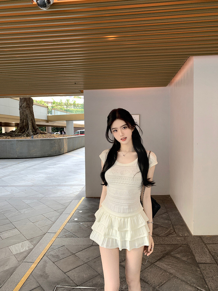 Woman wearing a white ruffled dress with lace detailing, standing outdoors under a striped ceiling.