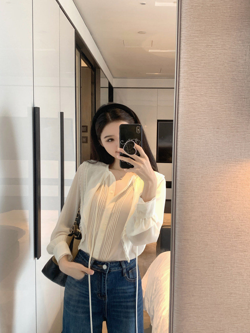 Woman taking mirror selfie wearing white blouse and jeans