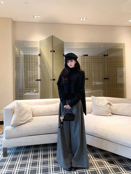 Woman wearing black turtleneck sweater, gray wide-leg pants, black beret, and holding small black bag