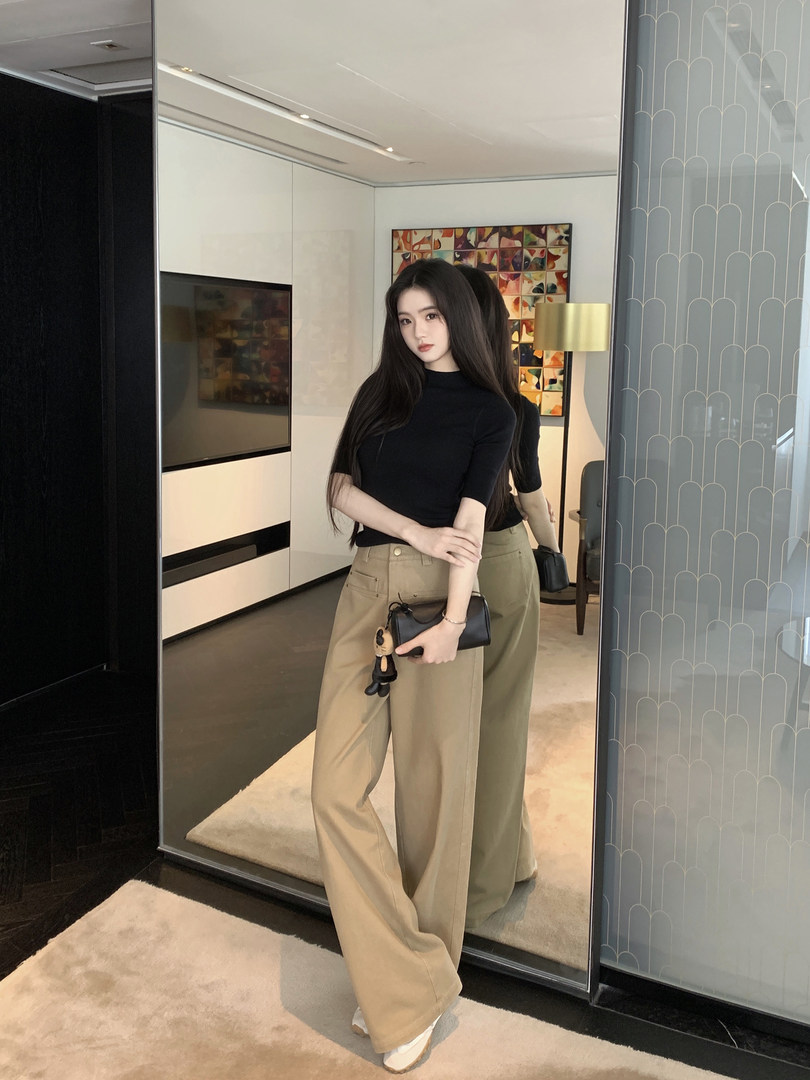 Woman wearing black top and beige wide-leg pants, holding a small black bag