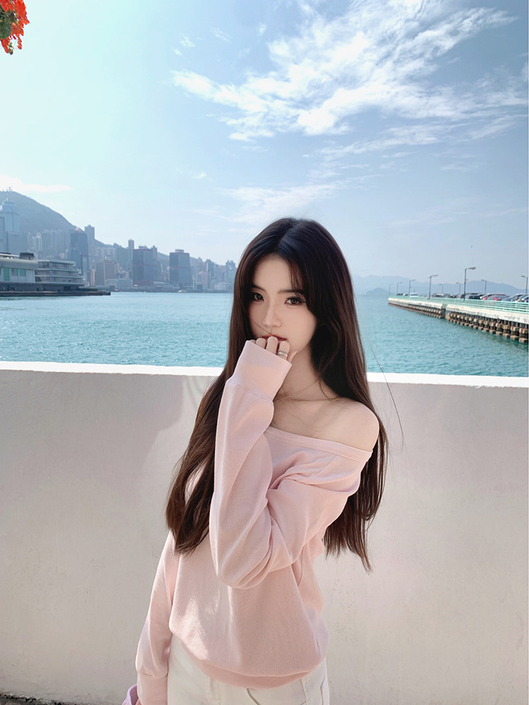 Woman wearing a pink off-shoulder top with a cityscape and waterfront background