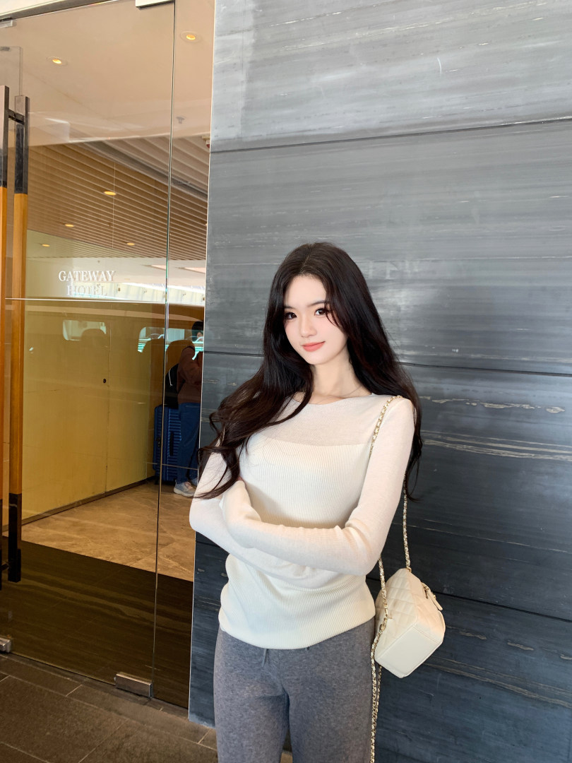 Woman wearing a cream ribbed long-sleeve top and gray pants, carrying a white quilted handbag.