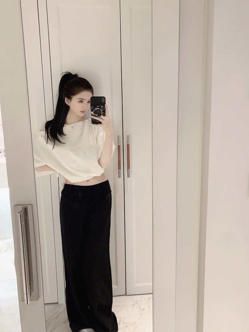 Woman taking mirror selfie wearing white off-shoulder crop top and black wide-leg pants