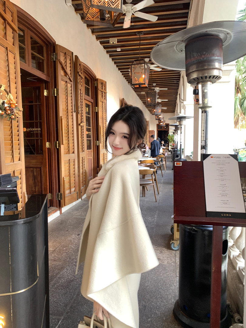 Woman wearing a cream-colored cape in an outdoor cafe setting