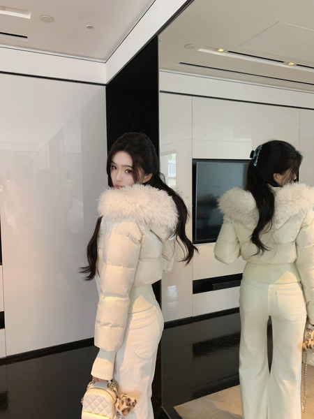 Woman wearing a white puffer jacket with fur collar and matching white pants, posing in front of a mirror.
