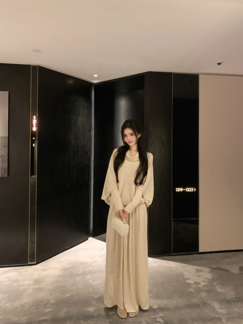 Woman wearing a beige long-sleeve maxi dress with matching bag, standing in a modern hallway