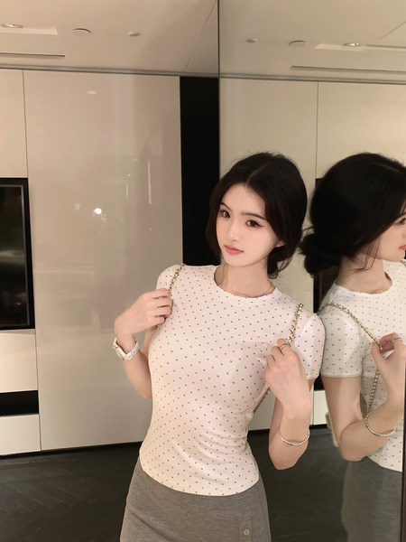 Woman wearing a white polka dot top with gray skirt, posing in front of a mirror.
