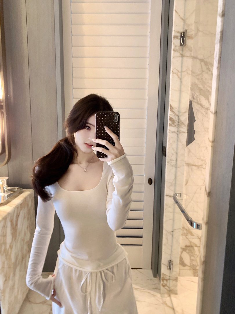 Woman taking mirror selfie wearing white long-sleeve top and matching pants