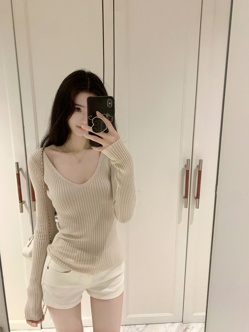Woman taking mirror selfie wearing beige ribbed long-sleeve top and white shorts