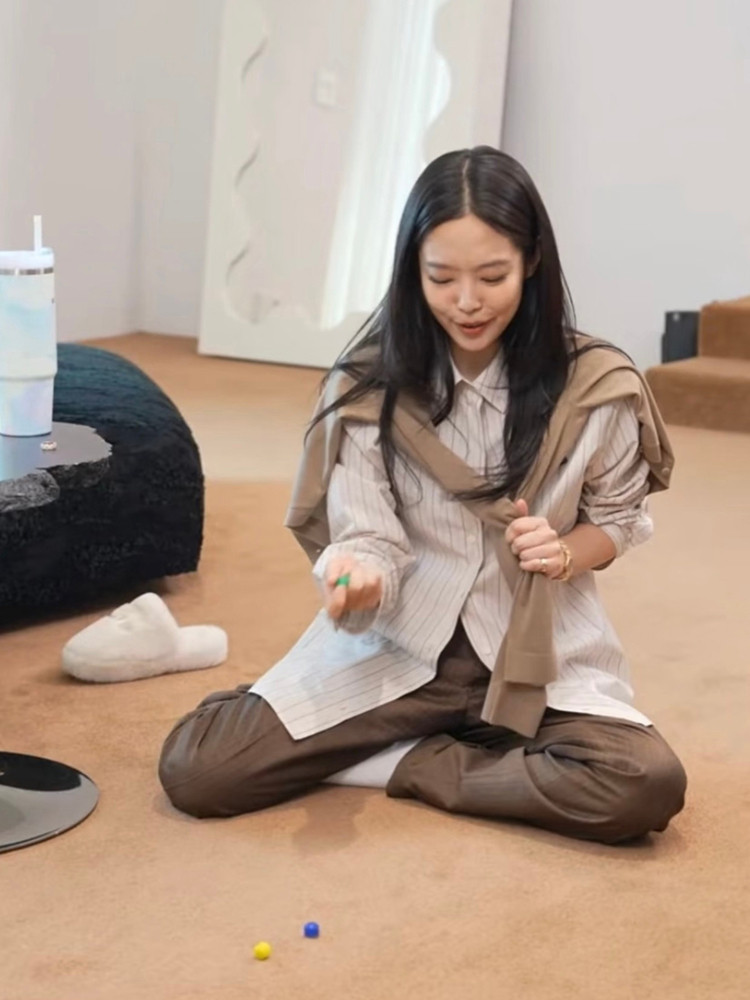 Woman sitting on the floor wearing a striped shirt and brown pants with a cardigan draped over her shoulders.