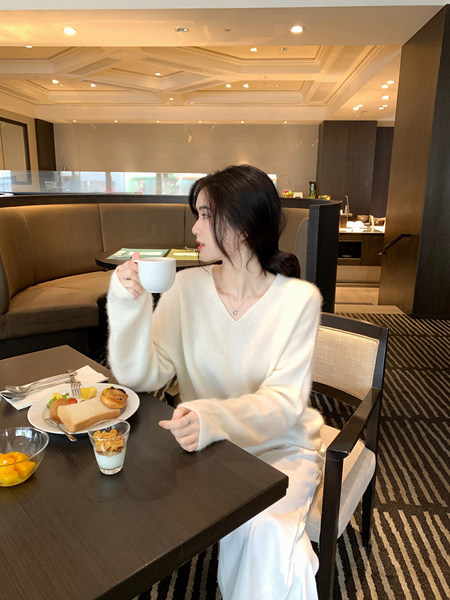 Woman wearing white V-neck sweater sitting at a cafe table with breakfast