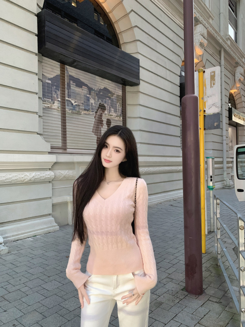 Woman wearing a pink cable-knit sweater and white pants outdoors.