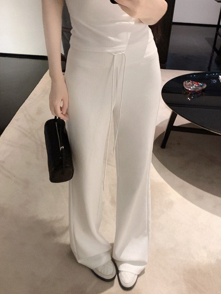 Model wearing white wide-leg pants with a drawstring waist, paired with white shoes and holding a black handbag.