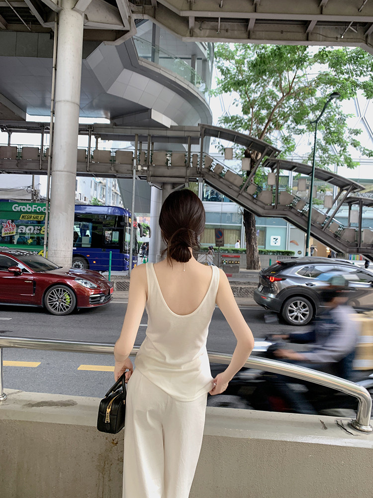 Woman wearing a white sleeveless top and matching pants, standing outdoors near a busy street.