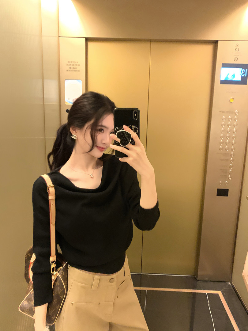 Woman taking mirror selfie in elevator wearing black top and beige pants with a designer bag