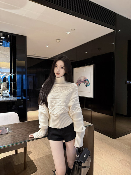 Woman wearing a white knitted turtleneck sweater and black shorts, holding a black handbag.