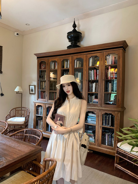 Woman wearing a white sleeveless dress and hat, standing in a room with bookshelves.