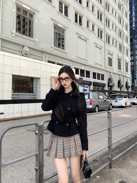 Woman wearing black coat and plaid skirt on city street